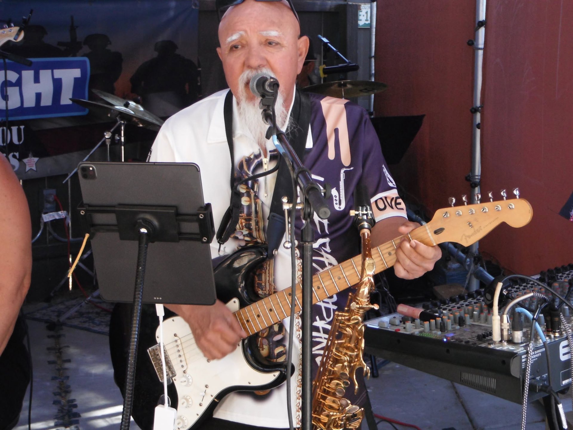Raul singing and playing Fender guitar with saxophone at his side