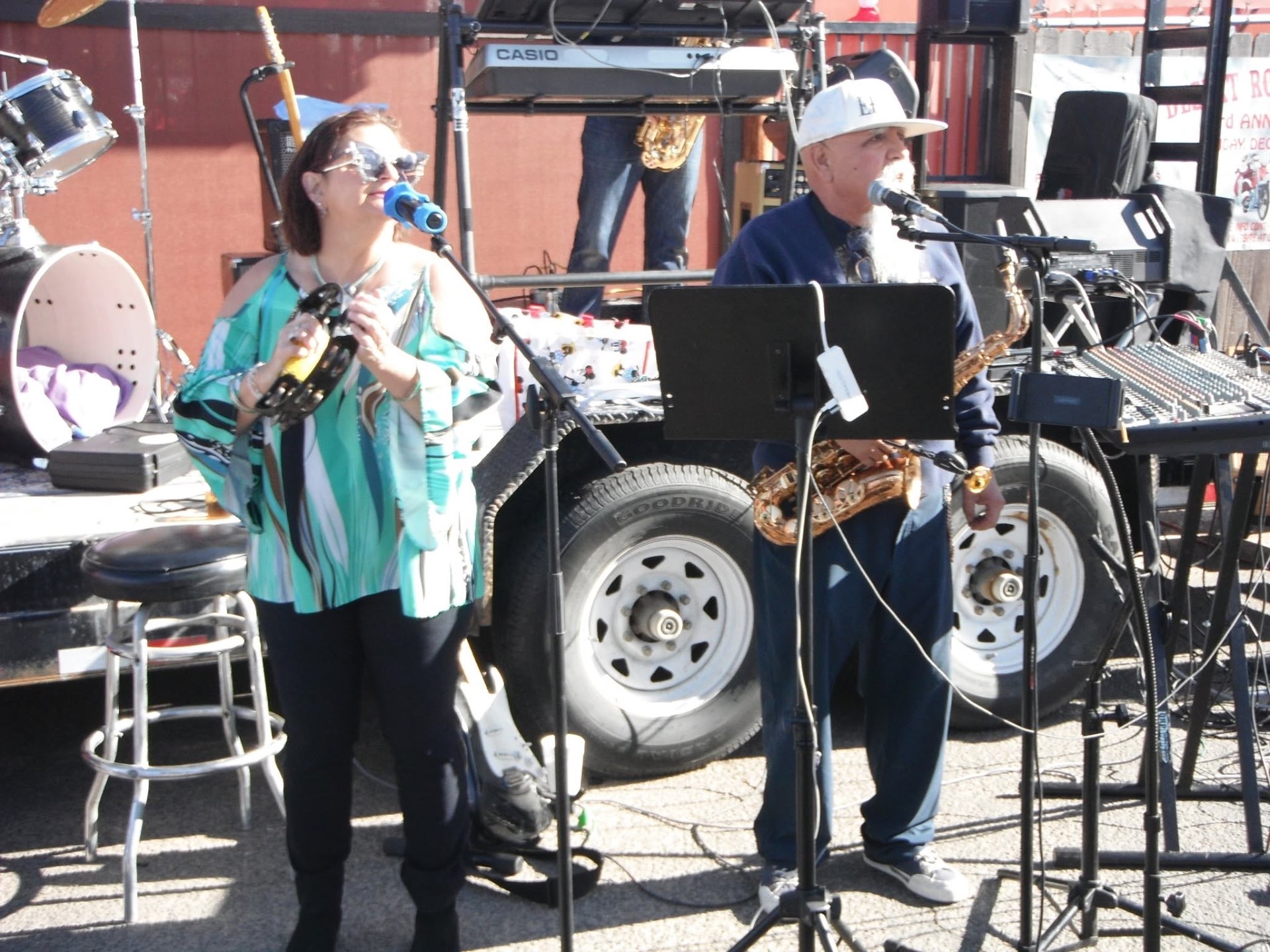 Laurie on tambourine and vocals beside Raul on saxophone at an outdoor event